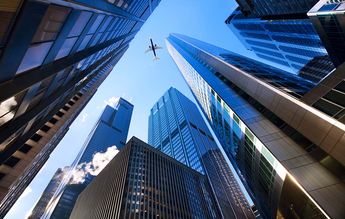 A plane flying over some skyscrapers in the sky.
